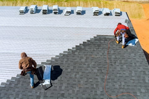 Worker hands installing roof shingles with air hammer