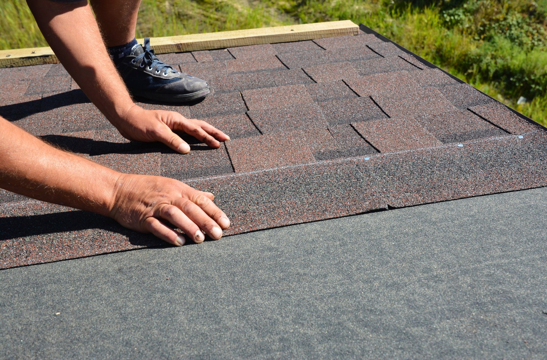 Roofing contractor laying asphalt shingles tiles on house rooftop