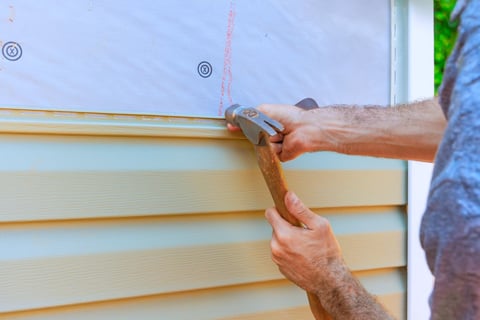 Worker installing vinyl siding on home renovation